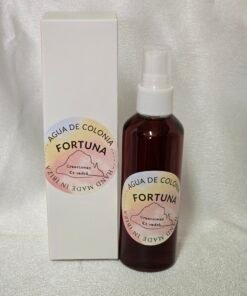 Botella de agua de colonia “Fortuna” de Creaciones Es Vedrà, hecha a mano en Ibiza, junto a su caja blanca sobre un fondo claro brillante.