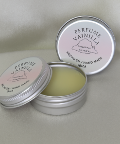 Perfume sólido con aroma a vainilla de Creaciones Es Vedra, presentado en envase metálico plateado con tapa rosa y texto “Hecho a mano en Ibiza”. Muestra el producto abierto sobre fondo suave, destacando su textura cremosa y estilo artesanal.
