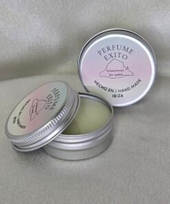 Dos envases metálicos de perfume sólido artesanal de la marca “Perfume Éxito”, uno abierto mostrando el contenido cremoso y otro cerrado. Ambos llevan la etiqueta con el logo de Creaciones Es Vedrà y la inscripción “Hecho en / Hand Made Ibiza”, sobre un fondo claro y brillante.
