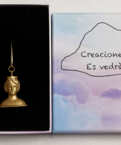 Pendientes dorados con forma de busto de la Diosa Tanit, presentados en una caja negra junto a un estuche con el logo de Creaciones Es Vedrà sobre fondo de tonos pastel.