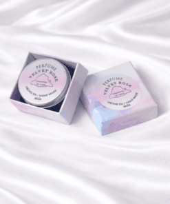 Perfume sólido Velvet Rose hecho a mano en Ibiza, presentado en caja pastel y envase metálico sobre fondo blanco de seda
